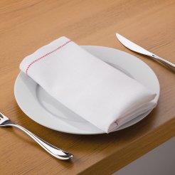 White linen tablecloth with a red hem, placed on a plate with cutlery on a wooden table.
